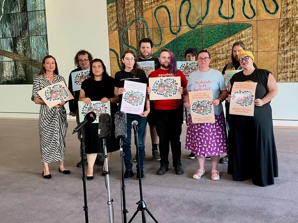 an image of a group of activists holding posters. the posters say "centrelink payments above the poverty line. Abolish 'mutual' obligations, with an illustration in the centre that reads "space to breathe, a moment to thrive"